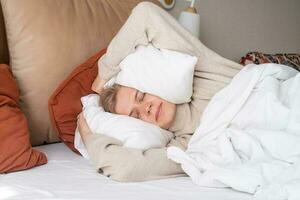 Woman sleeping at bed at home, covering ears with pillows from noise photo