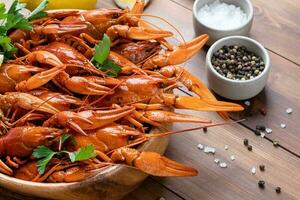 cooked crawfish in wooden bowl with lemons and spices on wooden background photo