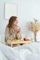 mujer sentado a cama a hogar Bebiendo café foto