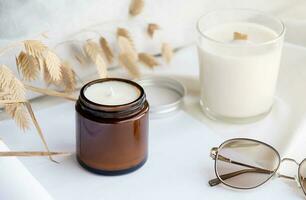 Soy wax aroma candle in brown jar on bed , with fashion glasses. Candle mockup design photo