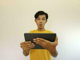 Surprised and excited asian man holding tablet isolated on white photo