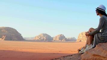 femme touriste en robe s'asseoir sur la falaise au point de vue sur le coucher du soleil dans le désert de wadi rum - vallée wadi saabit. Jordanie explorer le concept video