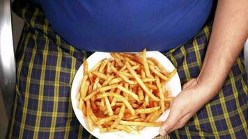 un grasa hombre comiendo francés papas fritas mientras situado video