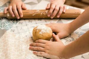 Children's hands prepare to use a rolling pin to roll ginger dough to bake Linzer cookies on the table in the kitchen. Lifestyle photo