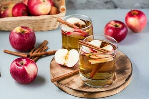 Fresh organic apple cider with cinnamon in glasses and apples on a gray background. Warming winter drinks photo
