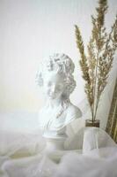 Plaster bust of a girl. Statuette on the background of light fabric and fluffy branches photo