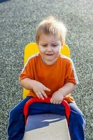 retrato de un chico. un niño es jugando en el patio de juegos. montando en el columpios contento niño. foto