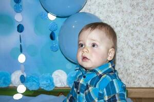 A beautiful baby is celebrating his first birthday. Portrait of the baby. A boy in a blue shirt among balloons and gifts. photo