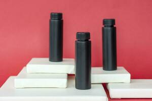 Black bottles of cream stand on white multi-level stands. Black bottles on a red background. Skin care, Moisturizing and nourishing or sunscreen. photo