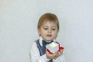 A little boy holds and hands over a red box, a Valentine's Day theme concept. Portrait of a cute boy in a suit with a bow tie. Valentine's Day. photo