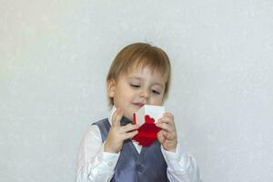un pequeño chico sostiene y manos terminado un rojo caja, un San Valentín día tema concepto. retrato de un linda chico en un traje con un arco atar. foto