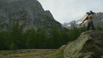 fotografo con tripode e telecamera su grande masso fra panoramico montagne video