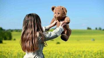 Kaukasisch meisje in masker met teddy beer dansen De volgende naar koolzaad veld- video