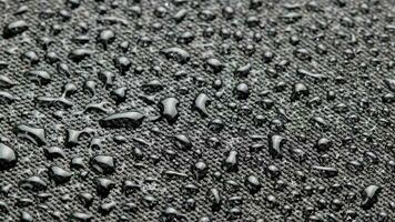 spinning closeup background of black hydrophobic fabric covered with water drops video