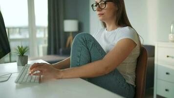 Casually dressed woman with headphones working with a computer and smartphone at home in a cozy environment. Remote work video