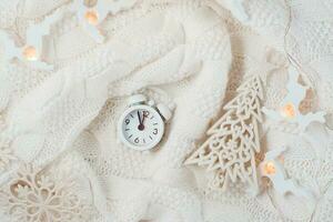 Countdown on Christmas night. Alarm clock, fir tree and candle on a knitted sweater. White colors. Top view. Copy space photo