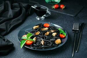 Ready-to-eat black spaghetti with mussels, tomatoes and basil on a plate on a black background. Food photography in dark colors photo