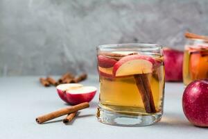 Fresh organic apple cider with cinnamon in glass and apples on a gray background. Warming winter drinks. Copy space photo