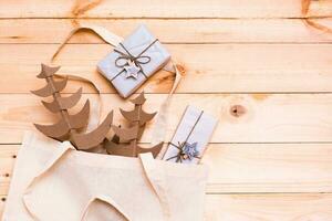 hecho a mano cartulina Navidad arboles y regalos envuelto en arte papel en un algodón compras bolso en un natural de madera antecedentes. Respetuoso del medio ambiente Navidad concepto foto