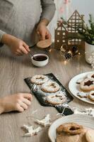 Children grease Linzer cookies with berry jam on the kitchen table. Cooking Christmas treats. Lifestyle. Vertical view photo