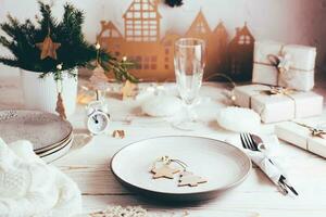 organización de un festivo Navidad mesa. lámina, cuchillería, champán vaso y Navidad decoraciones paisajes de mesa en blanco de madera mesa foto