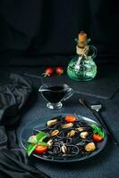 Ready-to-eat black spaghetti with mussels, tomatoes and basil on a plate on a black background. Food photography in dark colors. Vertical view photo