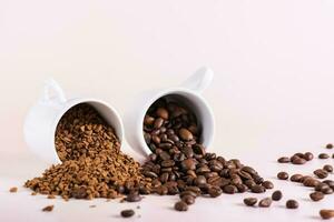 Dry instant coffee granules and roasted coffee beans are scattered from cups on the table photo