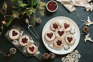 Ready Linzer cookies with berry jam on a plate and Christmas decorations on a dark background. Cooking Christmas treats. Lifestyle. Top view photo