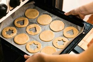 manos insertar un horneando sábana de crudo linzer galletas dentro el horno. Cocinando Navidad golosinas estilo de vida foto