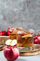 Fresh organic apple cider with cinnamon in glasses and apples on a gray background. Warming winter drinks. Vertical view photo