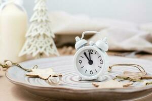 Concept Countdown on Christmas night. Table setting. Alarm clock five to twelve on a plate and christmas eco decorations on the table photo