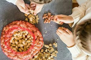 Peanut kernels, a mesh bag with unpeeled nuts and husks on the table. Children's hands are peeling nuts. Lifestyle. Top view photo