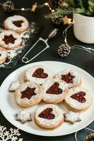 Ready Linzer cookies with berry jam on a plate and Christmas decorations on a dark background. Cooking Christmas treats. Lifestyle. Vertical view. Close-up photo