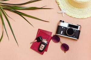 Summer bright travel flat lay with sunglasses, passports, car keys, vintage camera and straw hat on a beige background. Car travel. Top view photo