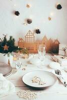 organización de un festivo Navidad mesa. lámina, cuchillería, champán vaso y Navidad decoraciones paisajes de mesa en blanco de madera mesa. vertical ver foto