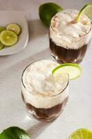 Alcohol free dirty soda cocktail of cola, whipped cream and lime in glasses vertical view photo