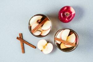 Fresh organic apple cider with cinnamon in glasses and apples on a gray background. Warming winter drinks. Top view photo