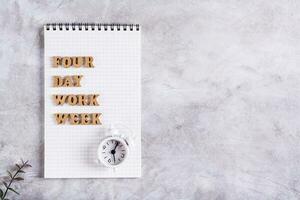 Four day work week concept wooden letters on notebook and alarm clock top view photo