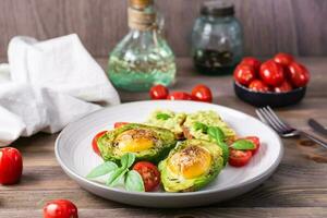 Hot appetizer baked avocado with egg, toast, cherry tomatoes and basil on a plate on a wooden table. Healthy eating. Flexitarian diet photo