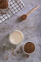Lactose free dietary buckwheat milk in a glass and seeds in a bowl top and vertical view photo
