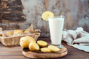 Alternative vegetable vegan potato milk in a glass and potato tubers side by side on a wooden table. Vegetarian food. photo