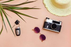 Summer bright travel flat lay with sunglasses, car keys, vintage camera and straw hat on beige background. Car travel. Top view photo