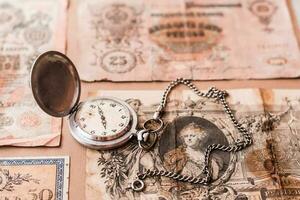 Old worn out of circulation ruble banknotes of tsarist russia and a watch on a chain on a brown background photo