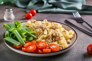 Pasta with minced meat, tomatoes and green onions on a plate on the table photo