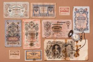 Old worn out of circulation ruble banknotes of tsarist russia and a watch on a chain on a brown background. Knolling top view photo