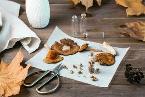 Dried chopped fly agarics stacked in a small jar and dry mushrooms on parchment and scissors on a wooden table. Microdosing and Alternative Medicine. photo