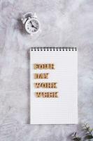 Four day work week concept wooden letters on notebook and alarm clock top and vertical view photo