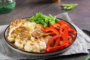 coliflor filetes con vegetales y hierbas en un plato en el mesa foto