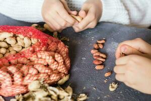 Peanut kernels, a mesh bag with unpeeled nuts and husks on the table. Children's hands are peeling nuts. Lifestyle photo