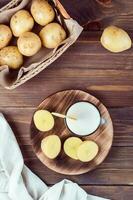 Alternative vegetable vegan potato milk in a glass and potato tubers side by side on a wooden table. Vegetarian food. Vertical and top view photo